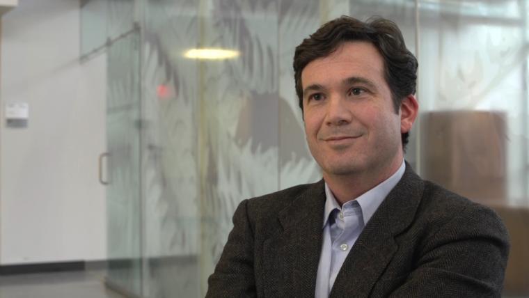 Head shot photo of Prof. Brady Deaton sitting in front of a glass wall