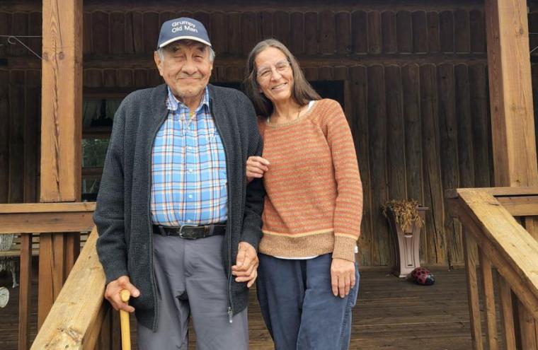 Sue stands with arm around Ray smiling on a wood deck