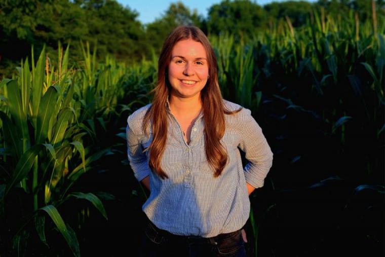 Kelly stands in front of green corn field smiling