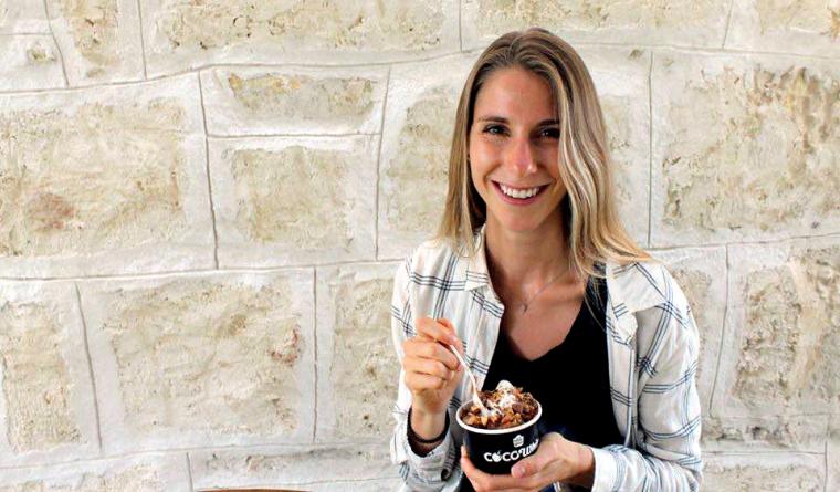 Kristi stands in front of a stone wall with a cup of food and a fork in her hand.