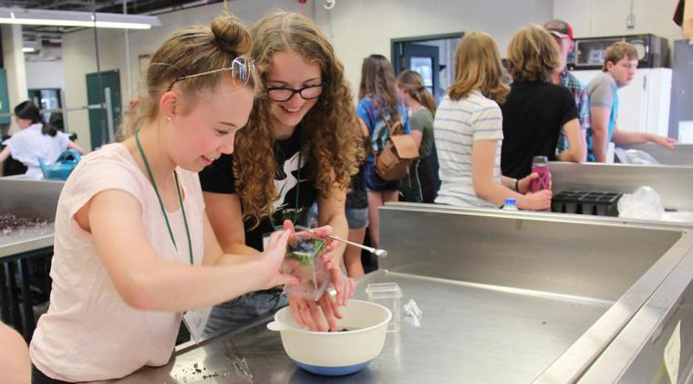 Two female students look at a plant in a lab setting