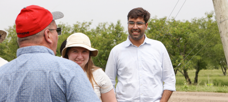 A group of students stand in a greenhouse research facility surrounded by tomato plants.