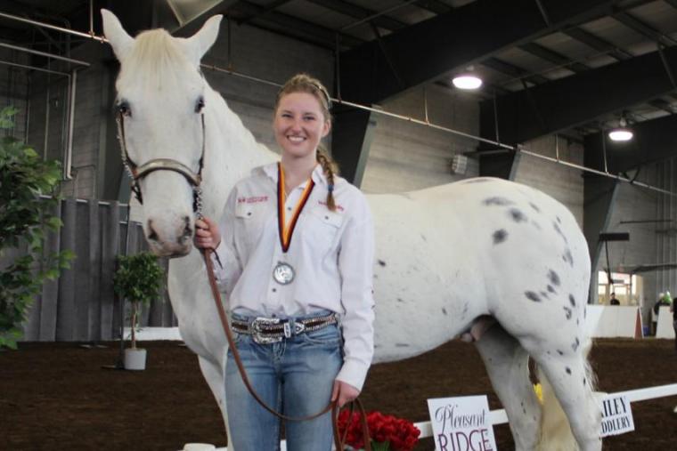 Female student stand with large white horse in a show ring