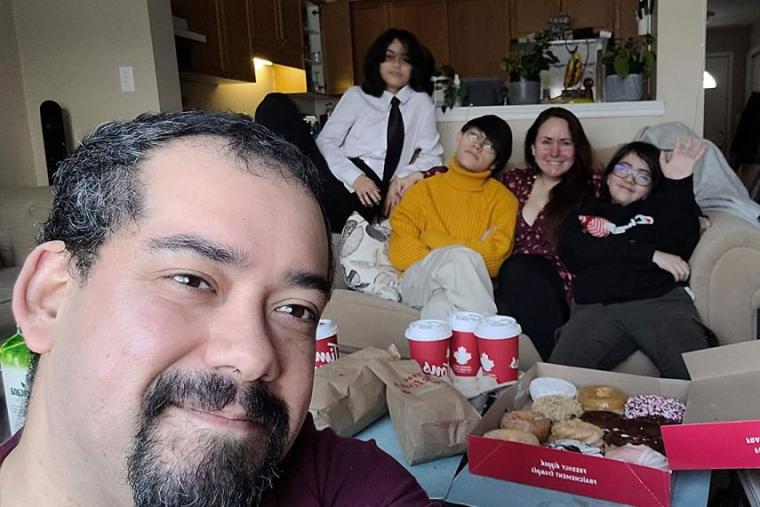 Selfie photo of Rod up close, his wife and three children sitting on couch behind him