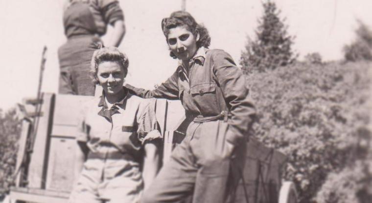 Rosalind and Erika stand together on a cart in work coveralls in 1942