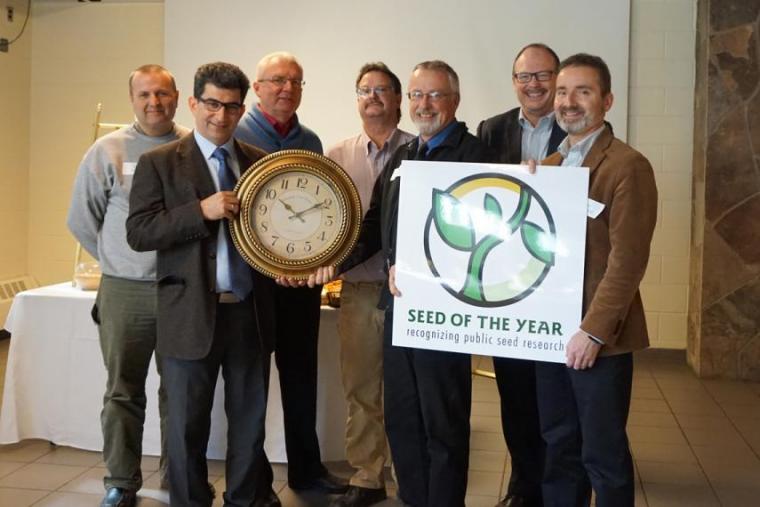 Seven men stand together with large award clock and sign that says Seed of the Year