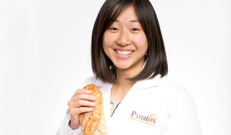 Head shot of Stephanie in a lab coat, holding bread.