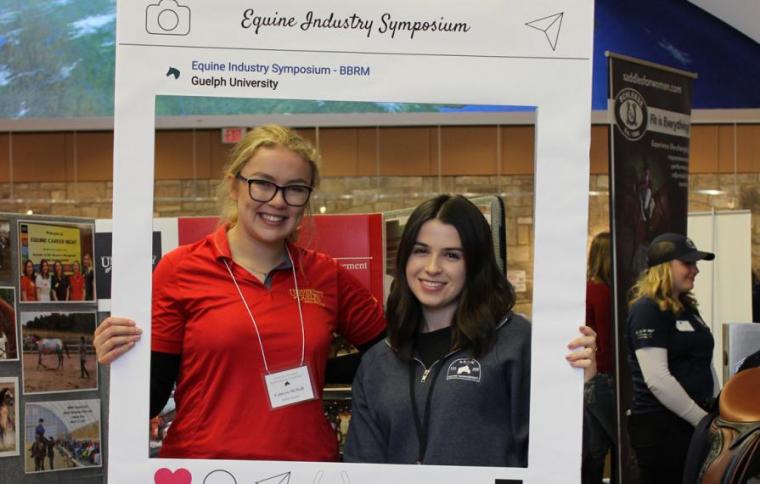 Two female students smile and pose with an Instagram frame