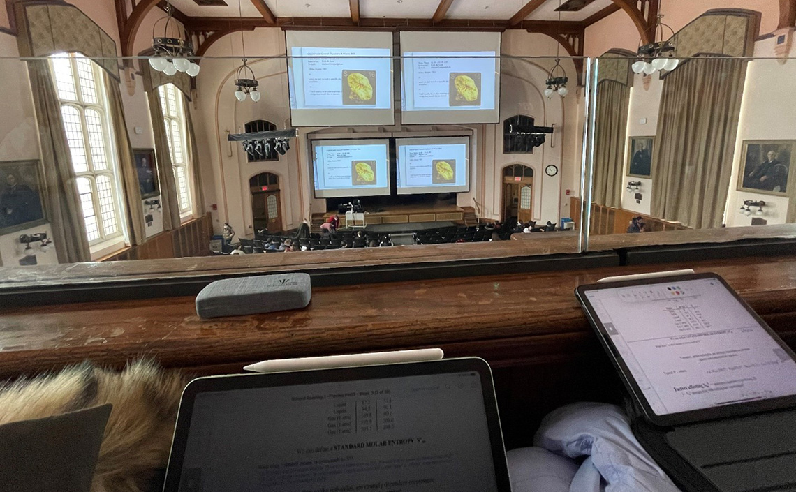 Students with computers in their lap sitting in the balcony of an old lecture hall. 