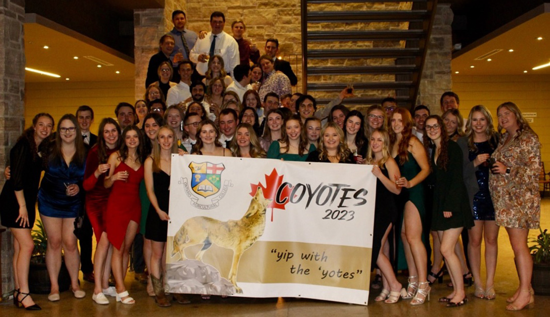 A large group of students posing behind a banner that says, "Coyotes 2023, yip with the yotes"