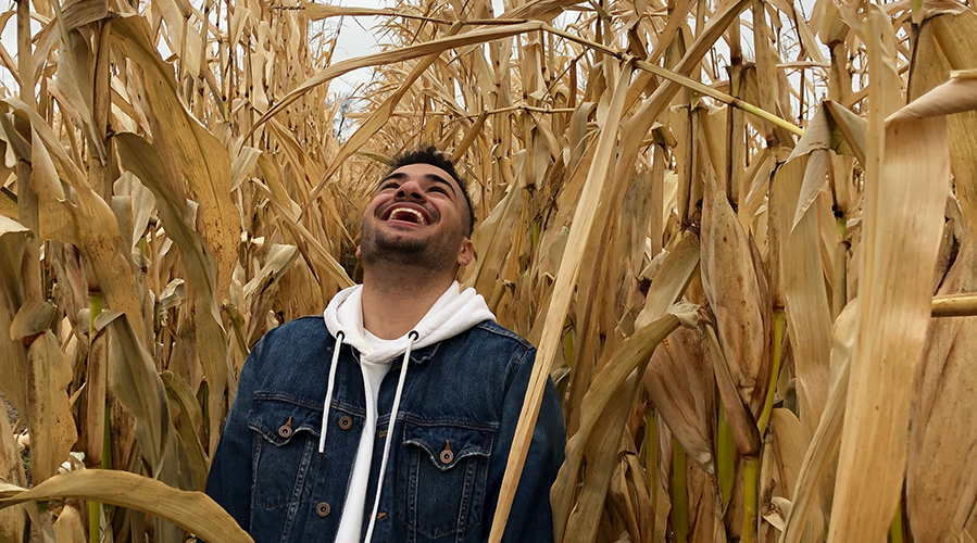 Ibrahim standing in a corn field, looking up at the tall corn with amazement. 
