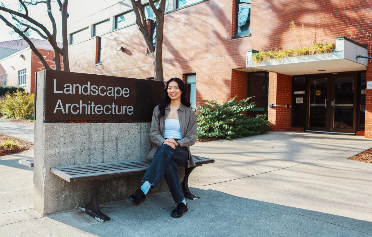 Landscape Architecture student Catherine Yan smiling for the camera while seated next to the Landscape Architecture building sign.
