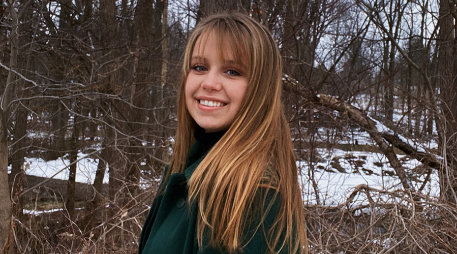 Emma standing on the edge of a forest in the winter.