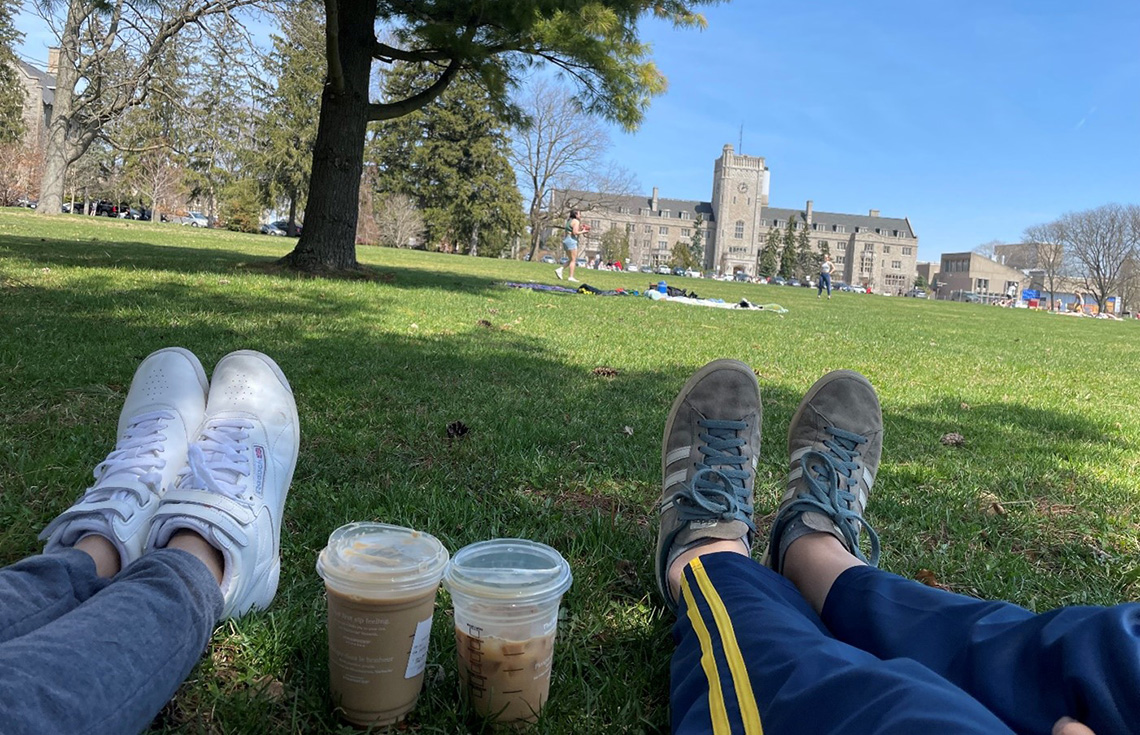 Two sets of legs with on a grassy field with Starbucks ice coffee.