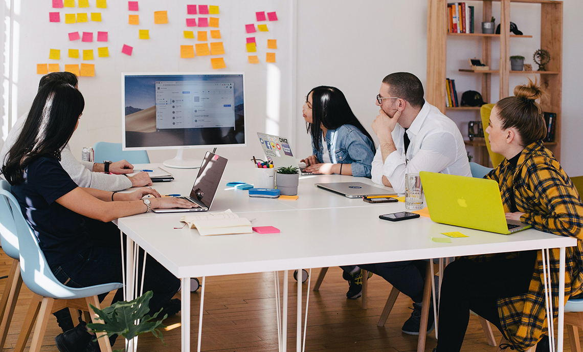 A group of students working at a table and looking at a white board full of sticky notes.