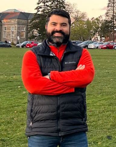 adrian correndo wearing a sweater and red shirt, standing in front of johnston hall