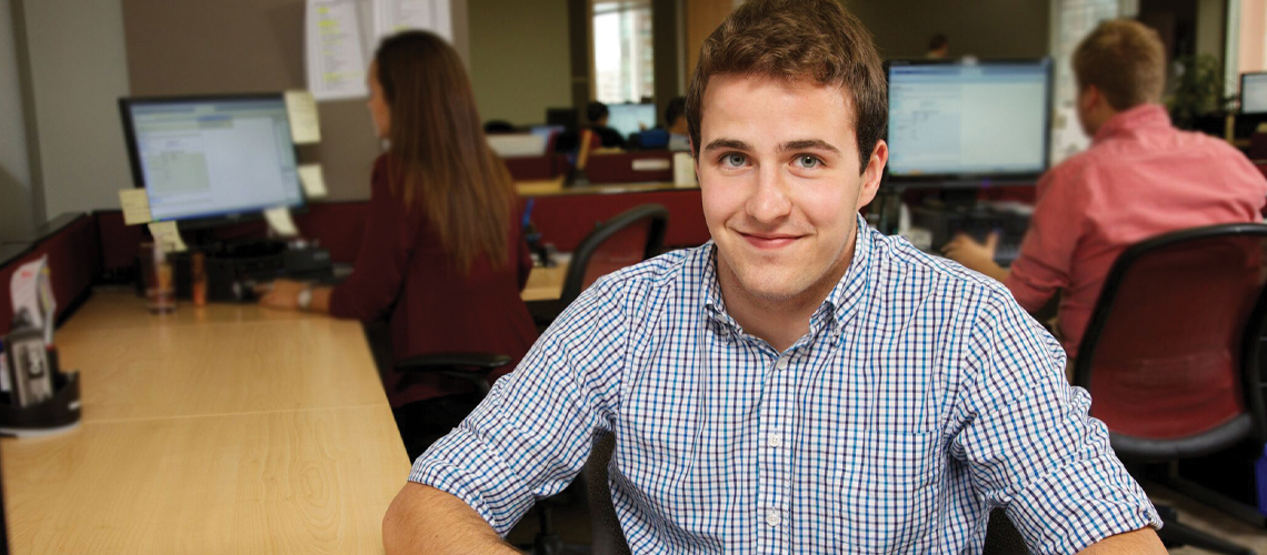 Male student sits at work desk smiling