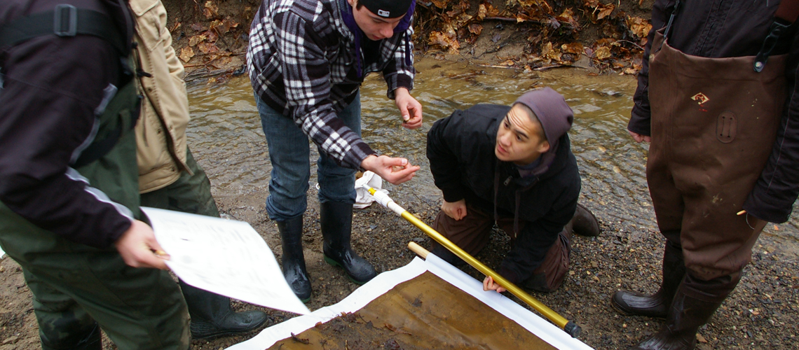 Student stand and crouch in river looking at papers and samples