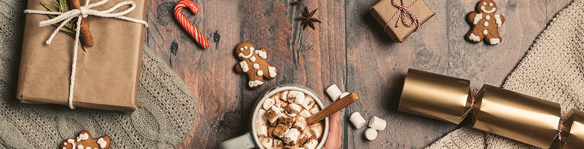 Image of a wrapped present, gingerbread cookies, candy cane, star anise, holiday cracker/popper, and a cup of hot cocoa.