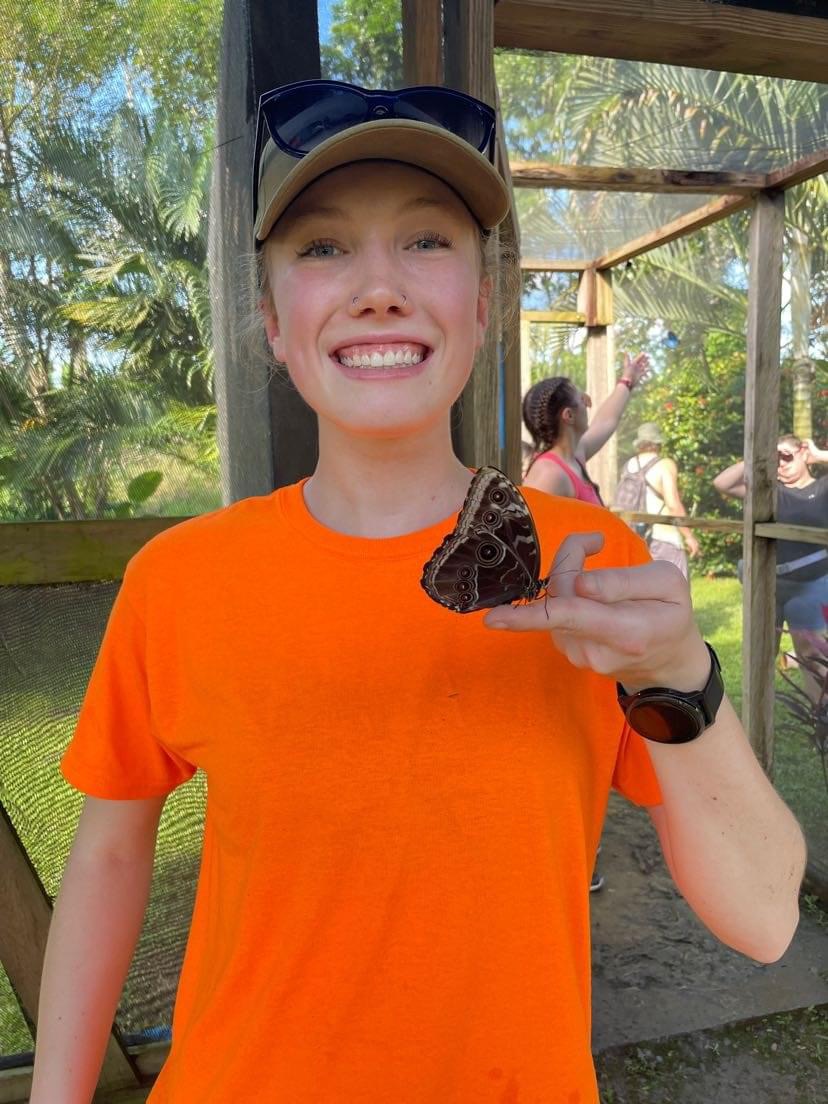 Lara-Nicole Cochrane smiling for the camera with a butterfly sitting on her finger.
