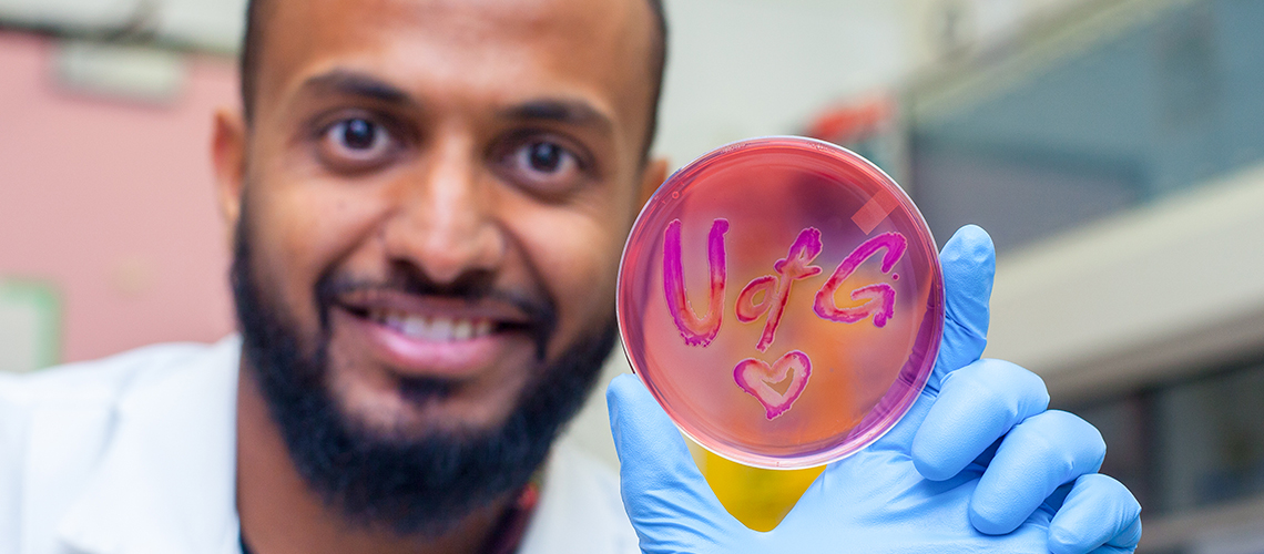 A student in a lab holds up a petri dish that says "U of G" with a heart.