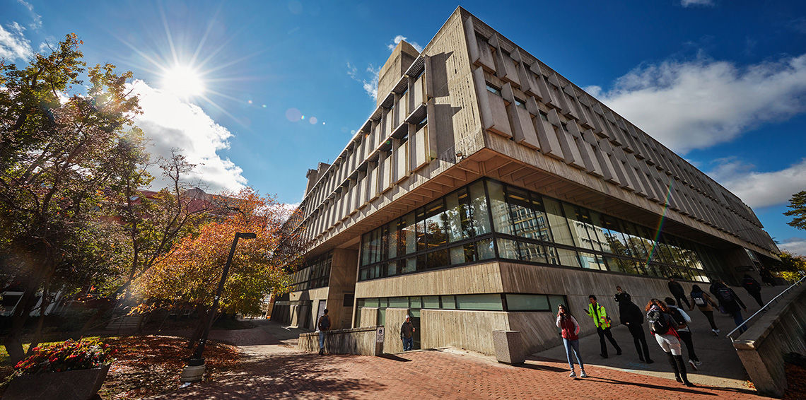 A wide shot of the library, a brutalist building with many large windows, on a bright, sunny fall day.