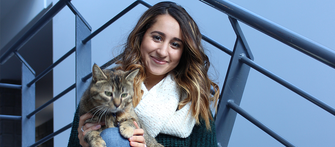 Female student sits on staircase with grey cat on her lap