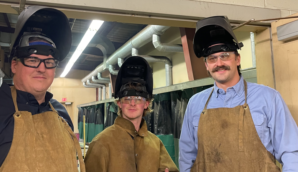wyatt and others in a barn wearing welding helmets and overalls