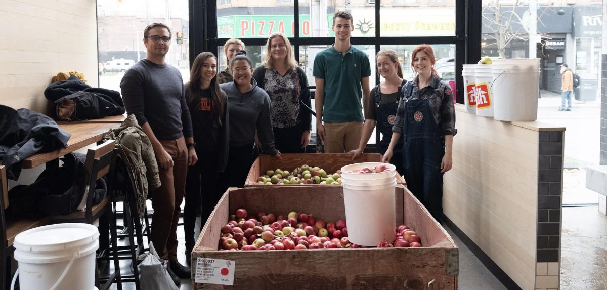 A group of people stand in front of a barrel of apples.