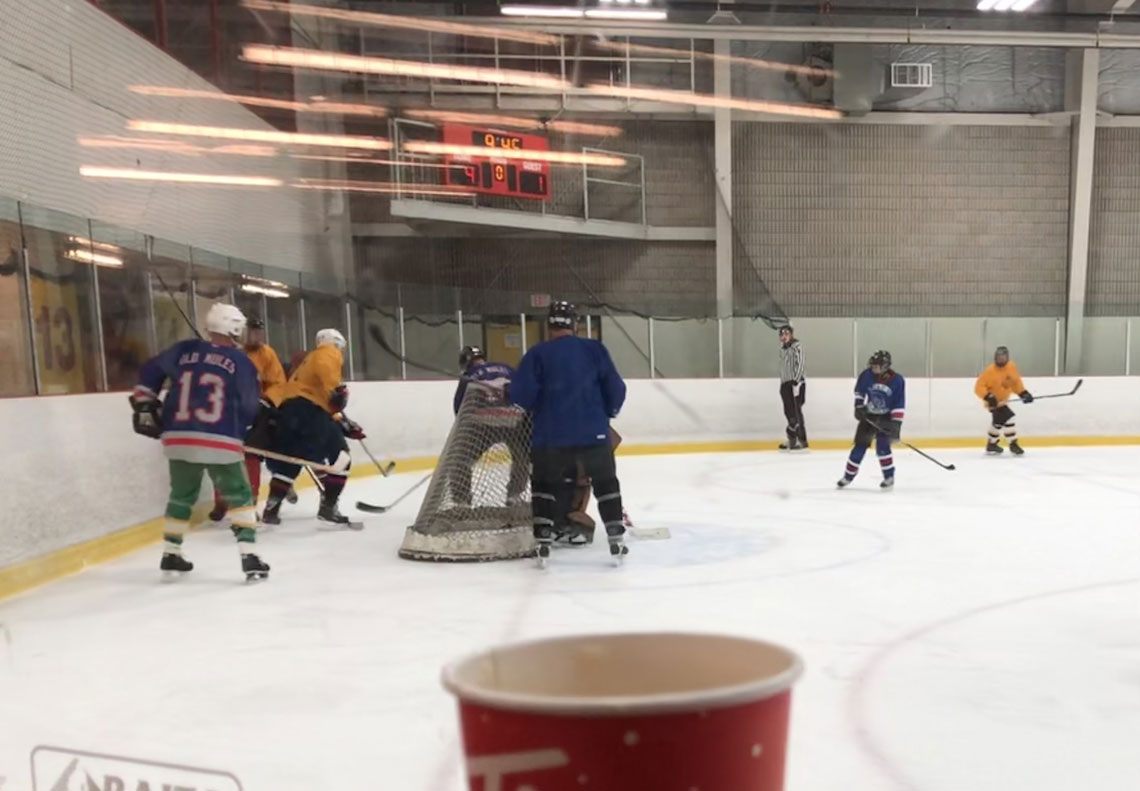 Hockey players gather around the back of a hockey net on the ice