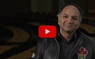 Head shot of Manish with a play button overlaid.