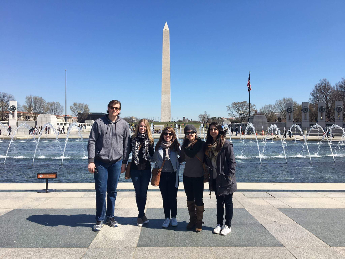 Five students stand in front of National WWII Memorial at the National Mall, water fountains in background