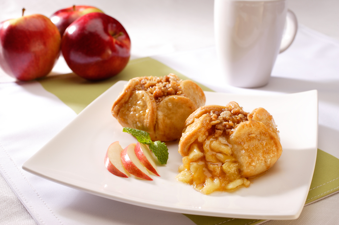 Two apple blossom desserts on a white plate with red apples in background