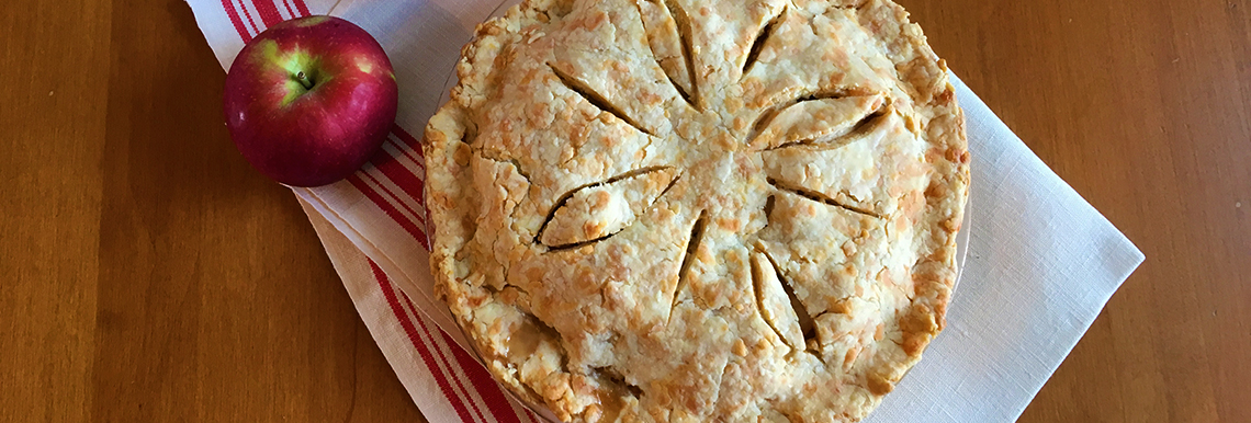 An apple pie sits on a table with an apple beside it.