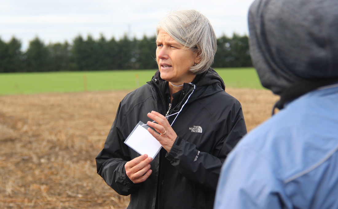 Claudia Wagner-Riddle stands outside in black jacket, field and trees behind her