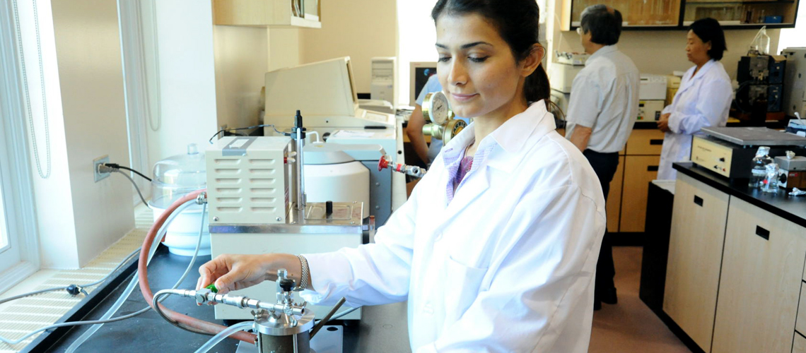 A student in a lab coat conducts an experiment in a lab. 