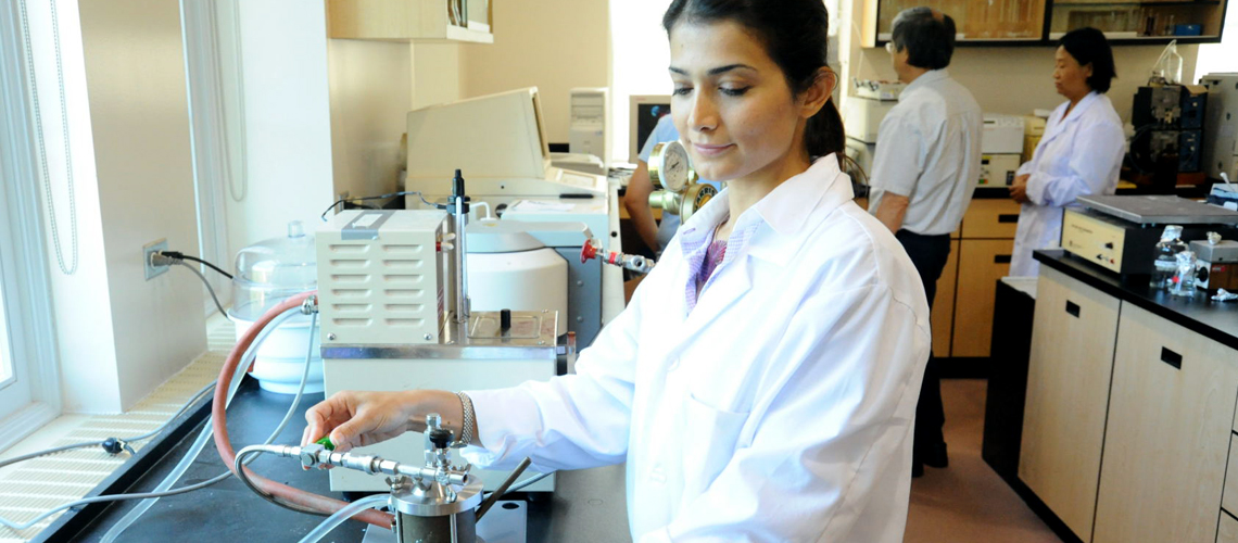 A student in a lab coat conducts an experiment in a lab.