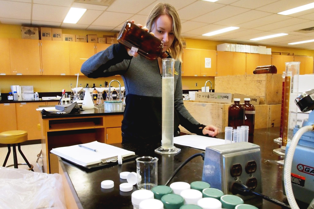 Haley pours liquid from a brown bottle into a graduated cylinder.