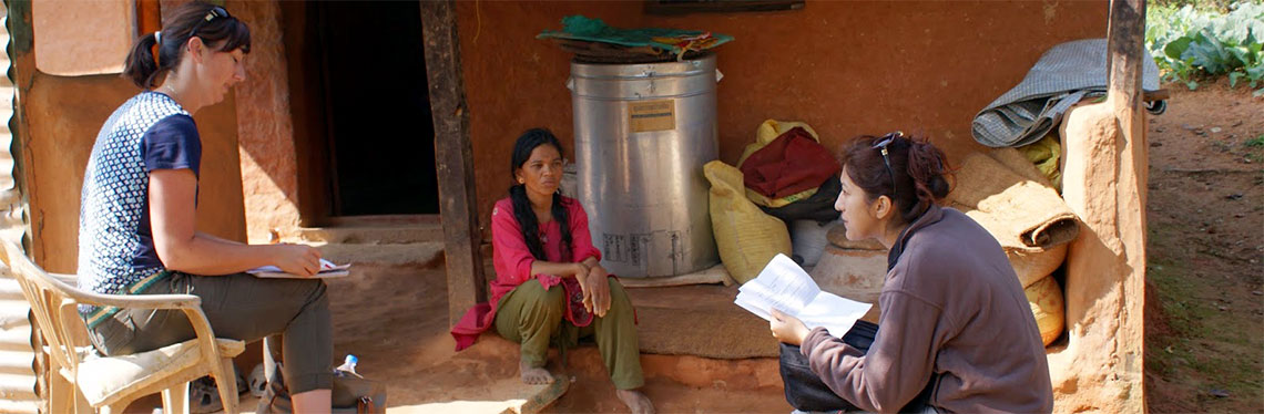 Ashley sitting in chair outside of Nepali home, interviewing female farmer with translator