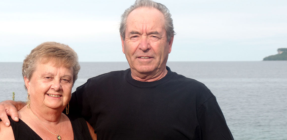 Barb and Murray Mielhausen stand together in front of a lake. 