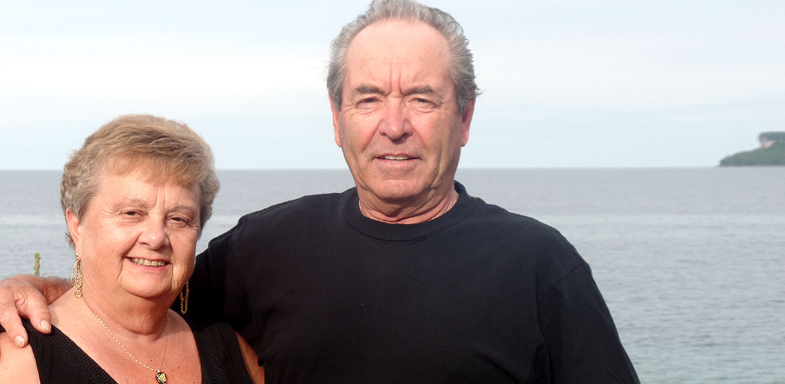 Barb and Murray Mielhausen stand together in front of a lake.