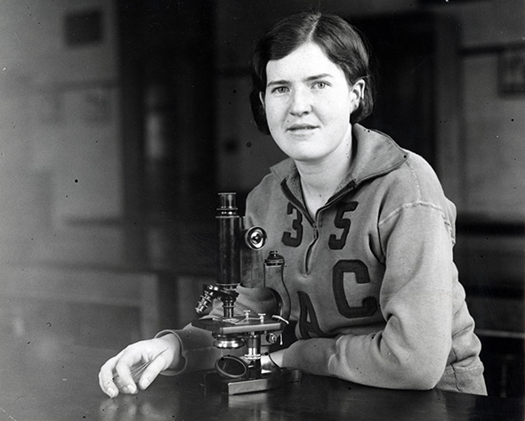 Helen Quinn in 1935 sitting at desk with a microscope
