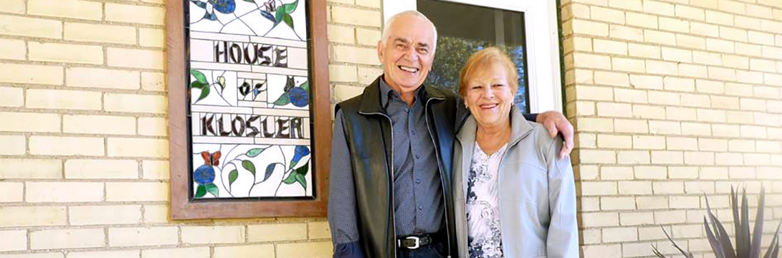 George and Gerri Klosler stand outside of their yellow brick home