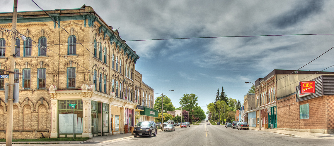 Photo of a car-lined street with old building on left and CIBC bank on right.