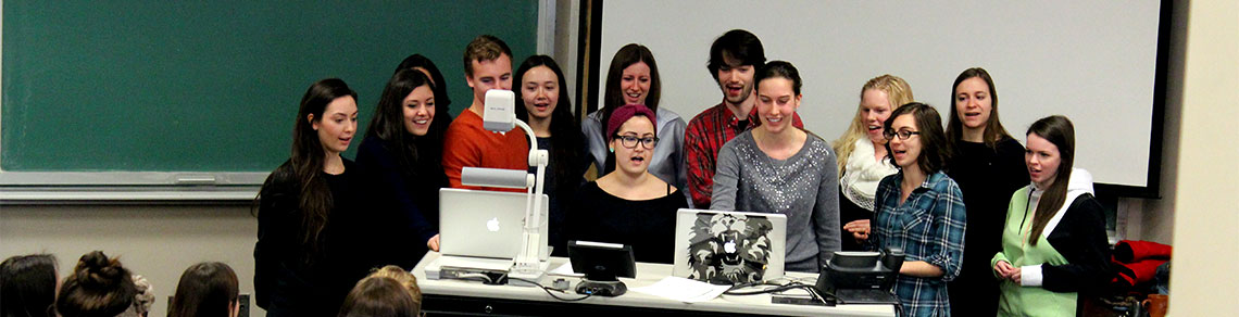 Group of students stand at front of lecture room singing