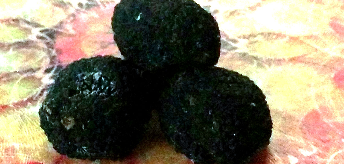 Three dark coloured truffles piled on a bright plate.