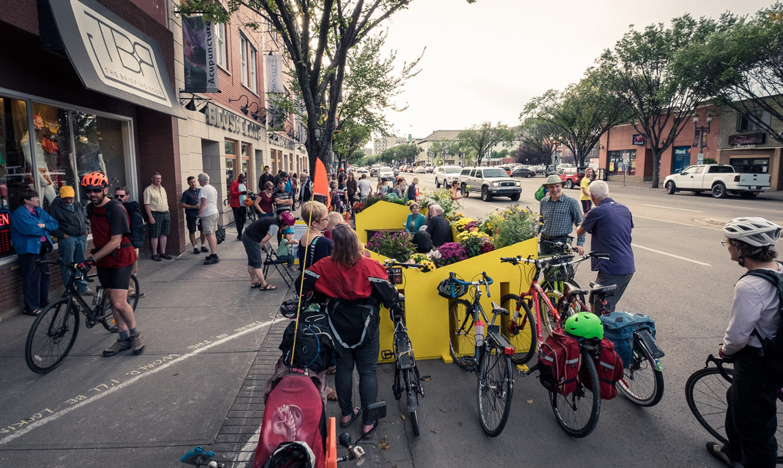 Bikes and people gathered together around a yellow seating structure on the side of city street
