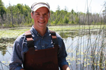 Joshua Persi stands in overalls in a large pond.