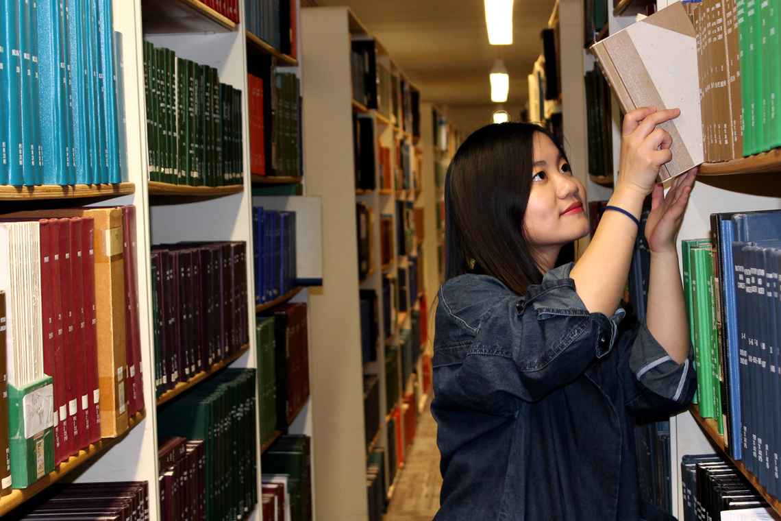 Xinya pulls a book from a shelf at the library.
