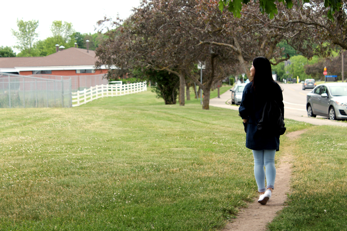 Xinya walks along a small dirt path near a road.